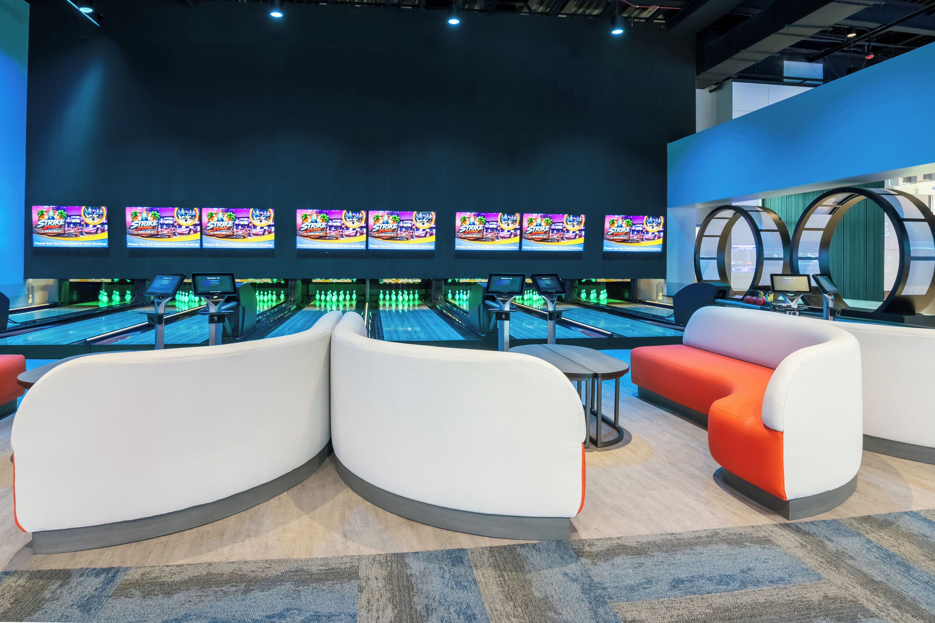 A bowling alley with multiple lanes, seating areas, and overhead monitors displaying bowling games.