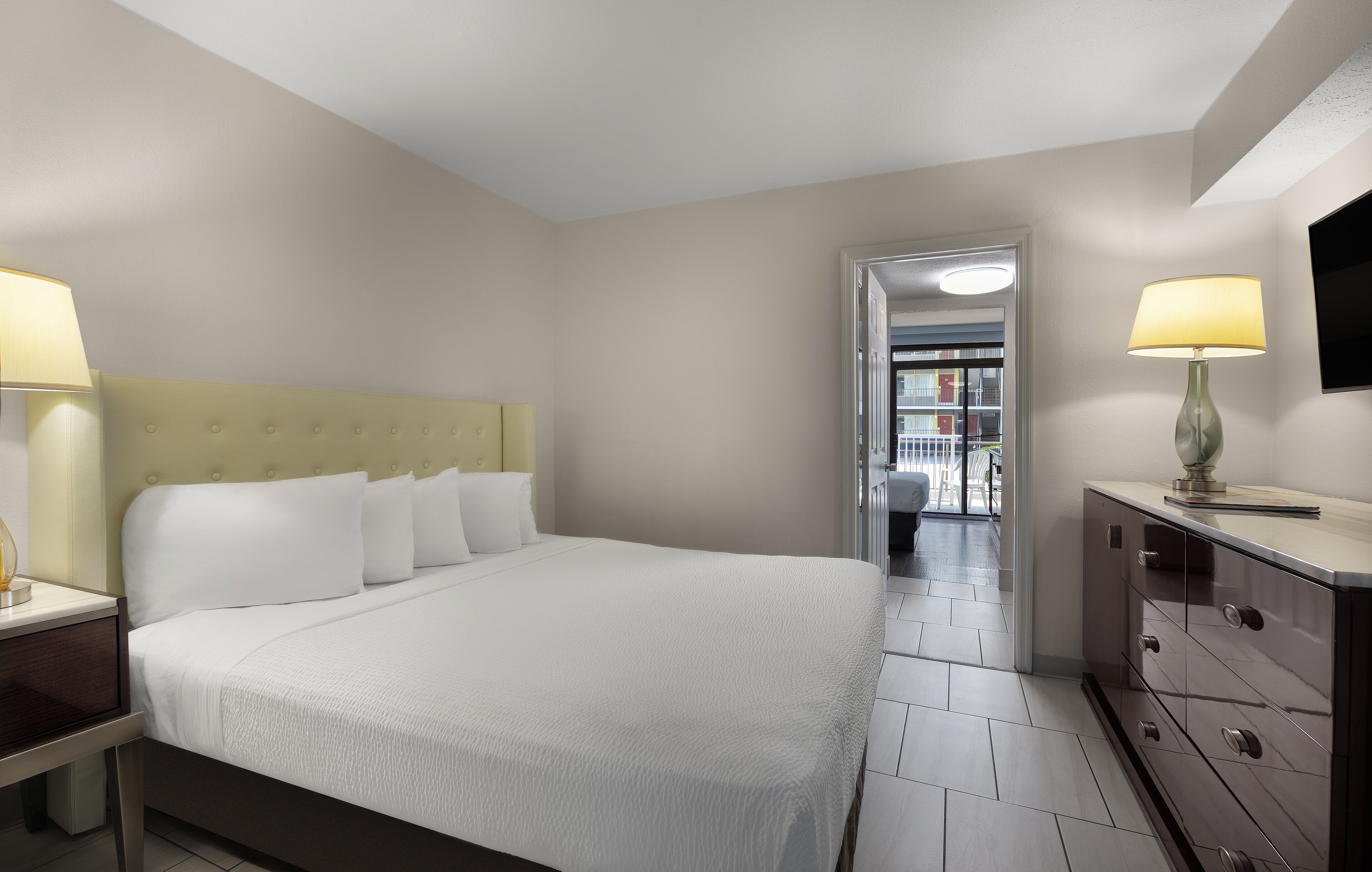 A hotel room with a large bed, bedside lamps, a dresser, and a TV mounted on the wall.