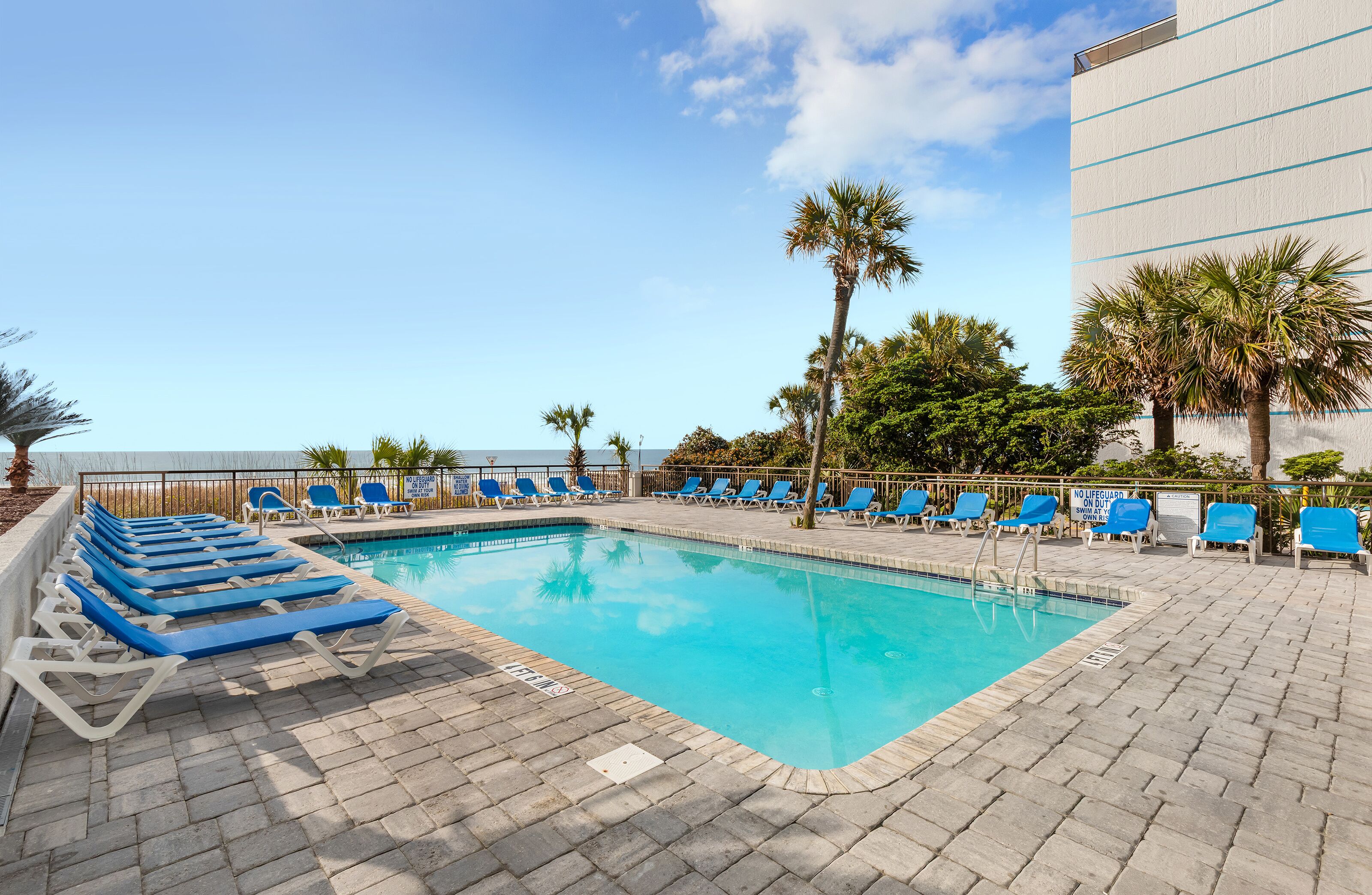 A swimming pool with blue lounge chairs and palm trees.