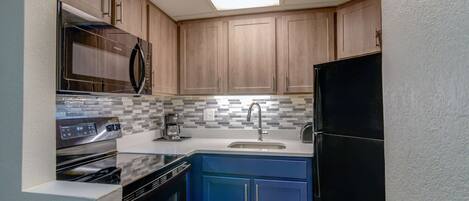 A compact kitchen with wooden cabinets, a microwave, a stove, and a sink.
