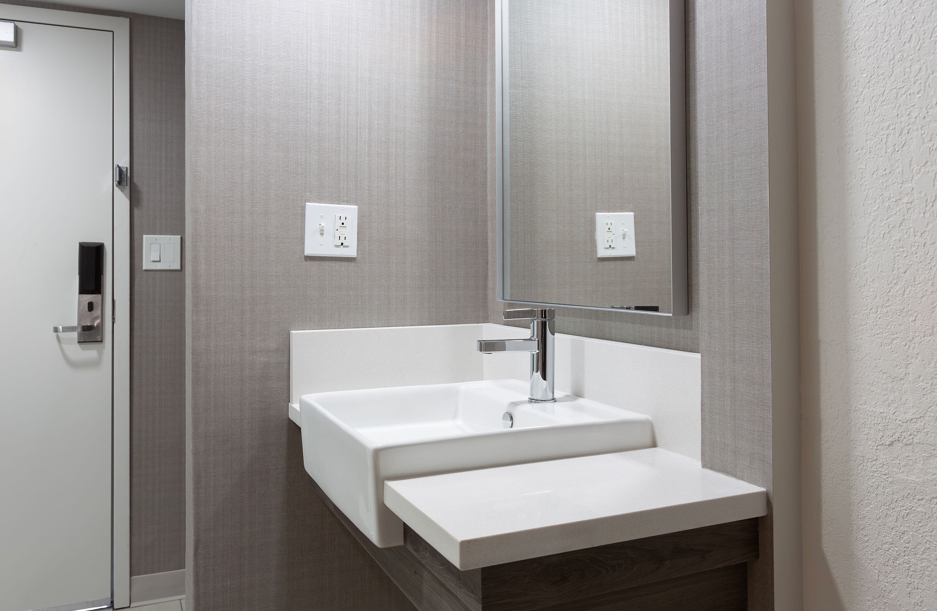 A modern bathroom with a white sink, a large mirror, and a wooden vanity.