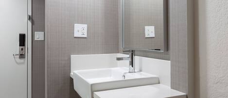 A modern bathroom with a white sink, a large mirror, and a wooden vanity.