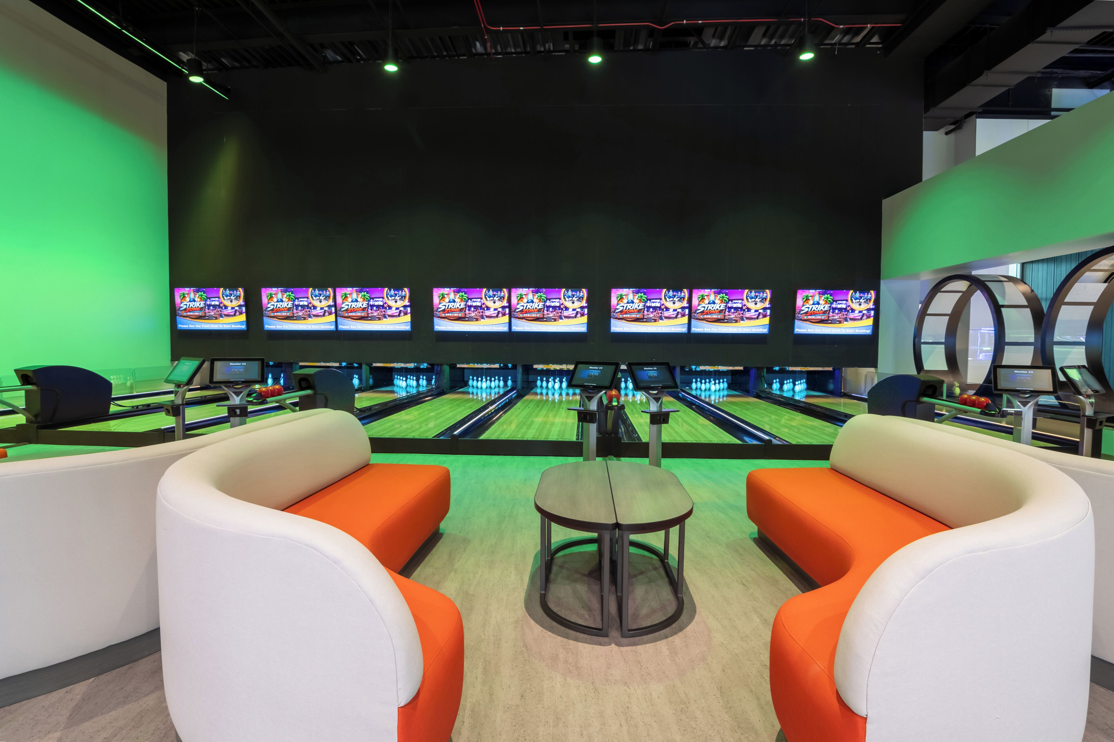 A bowling alley with multiple lanes, bowling balls, and pins. There are several screens displaying a bowling game.
