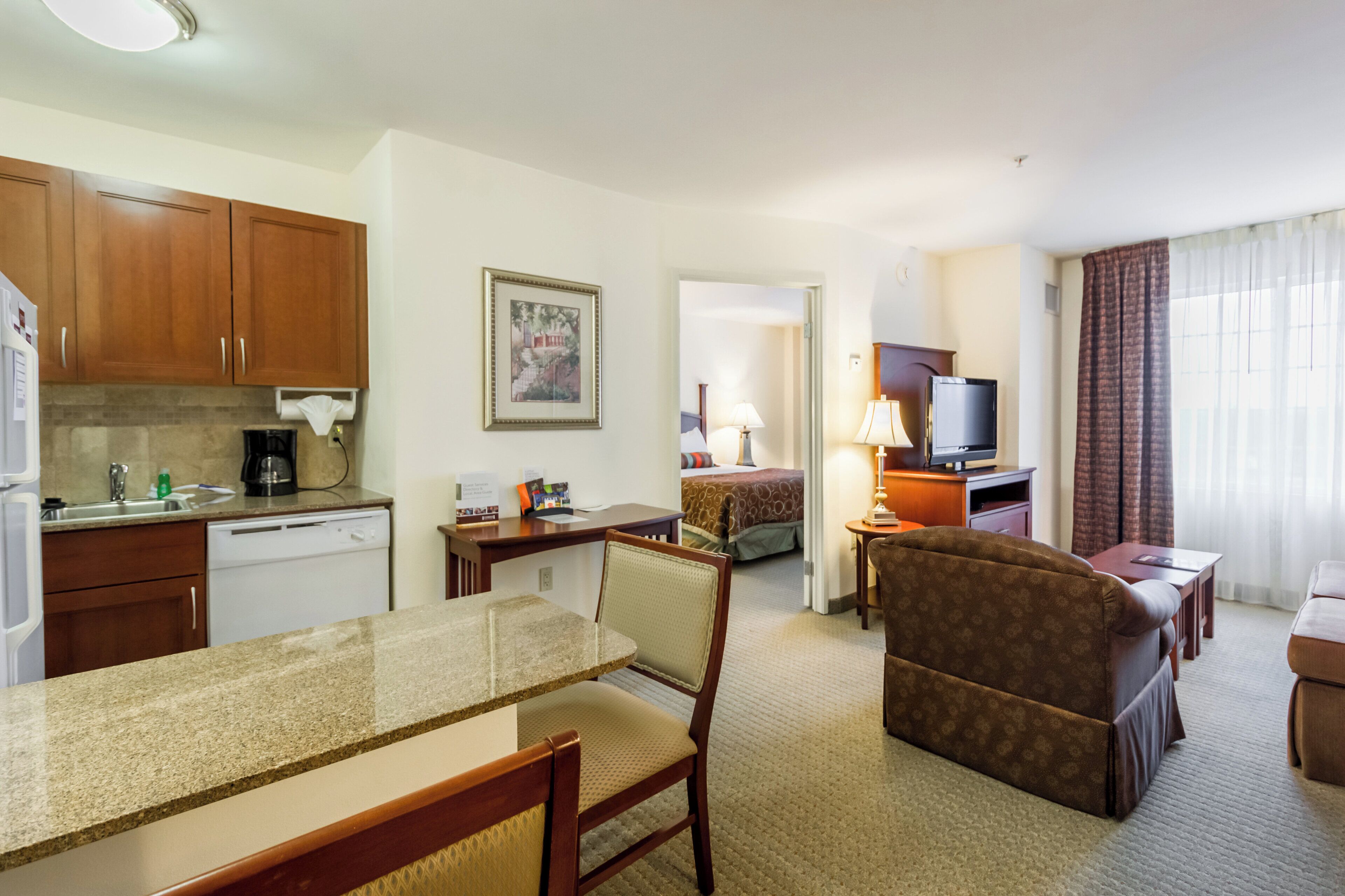 A hotel room with a kitchenette, a dining area, a bed, a TV, and a seating area.