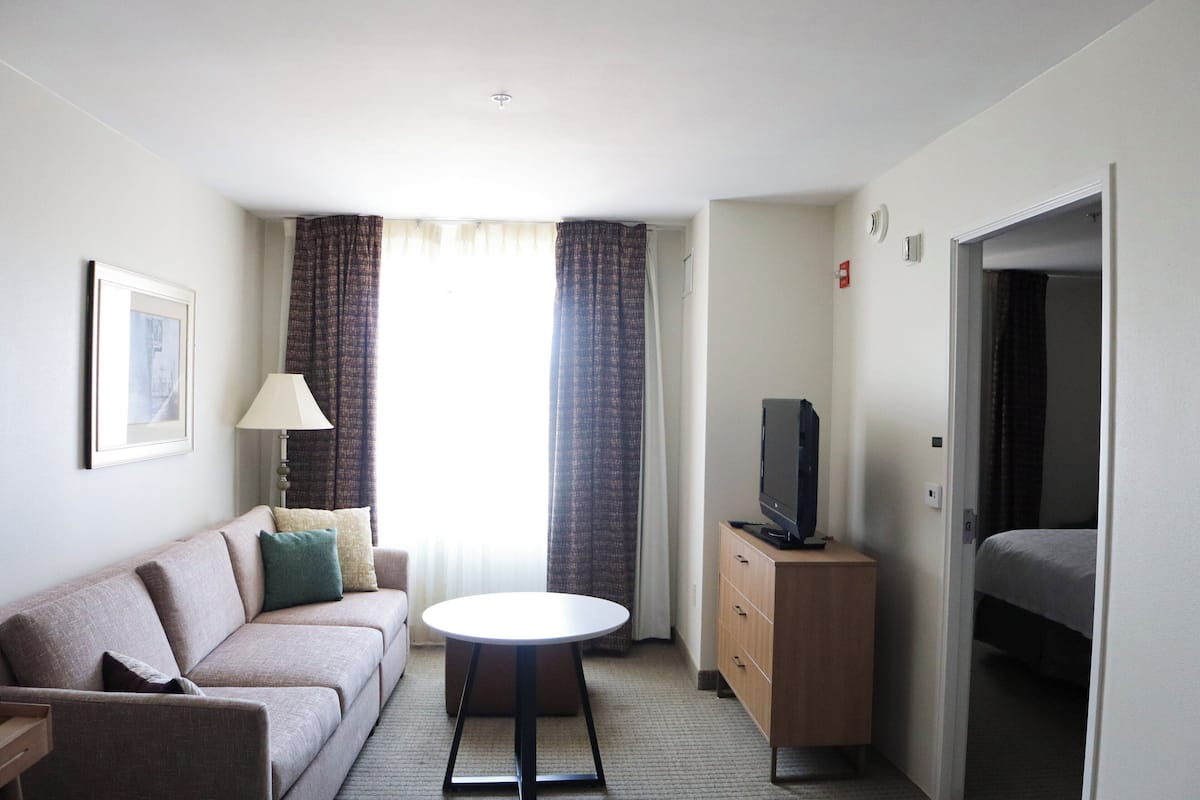 A hotel room with a sofa, a small round table, a TV on a wooden cabinet, and a bed.