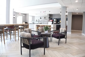 A modern lounge area with seating, a coffee station, and a visible kitchen area in the background.