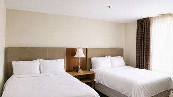 A hotel room with two beds, a nightstand, a lamp, and a window with curtains.