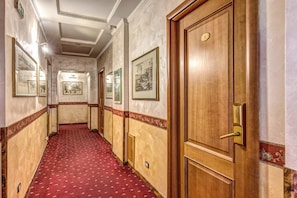 A hotel hallway with framed pictures on the walls, wooden doors, and a red carpeted floor. - Hotel Giuliana (Rome)