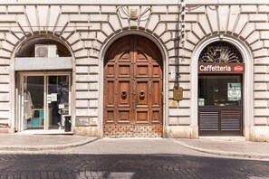 Een gevel met een grote houten deur, een glazen ingang en een bordje met de tekst 'Caffetteria'.