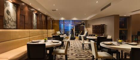 A modern dining area with a checkered floor, round tables, and cushioned seating.