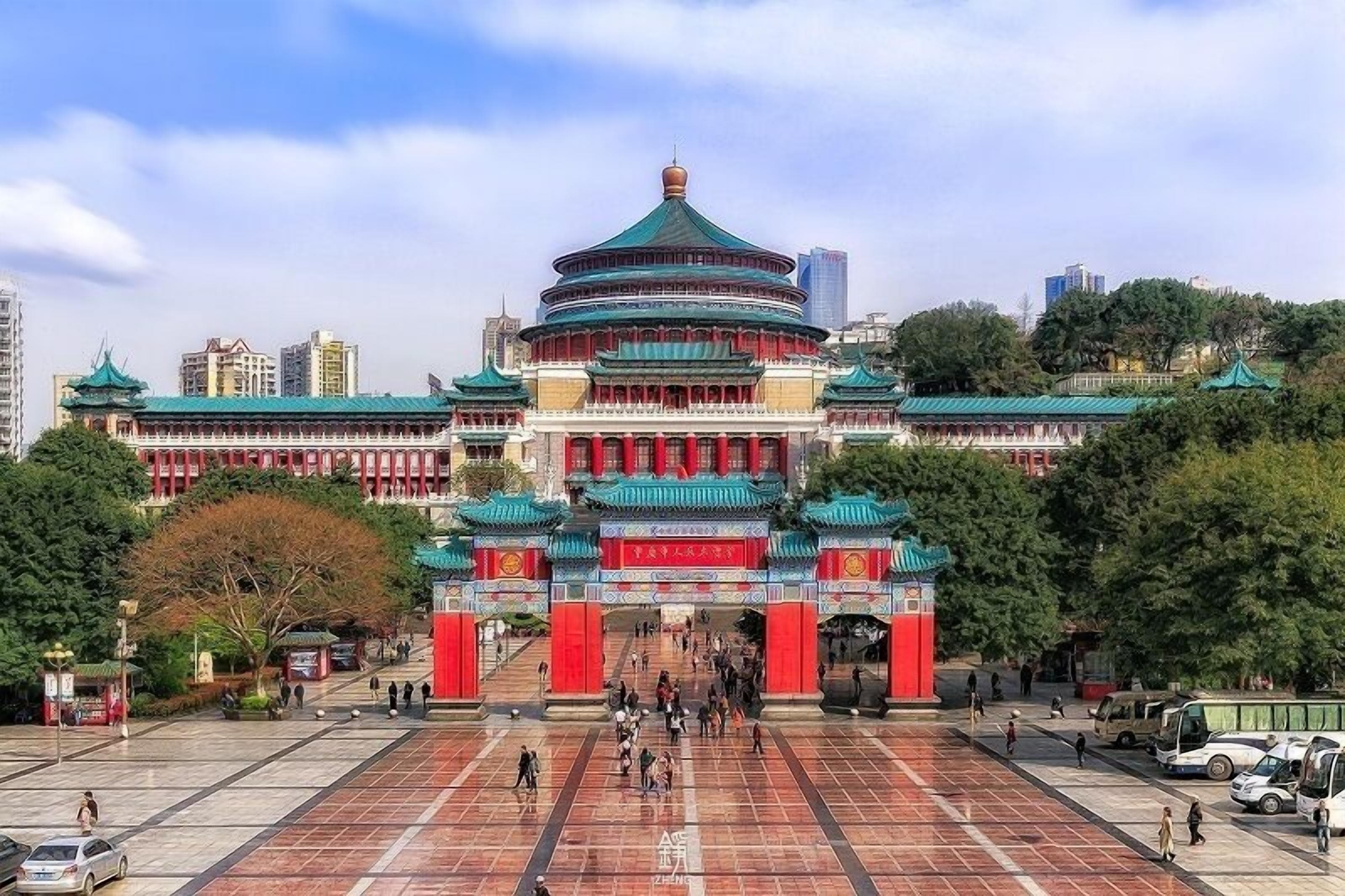 A traditional Chinese building with a circular main structure, red and green roof, and a large open plaza in front.