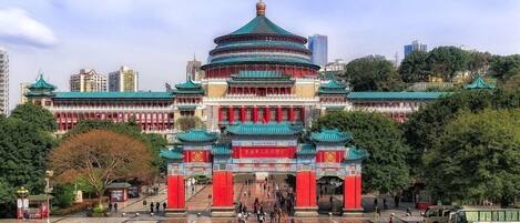 Een traditioneel Chinees gebouw met een rond hoofdgedeelte, een rode en groene dakbedekking en een groot open plein ervoor.