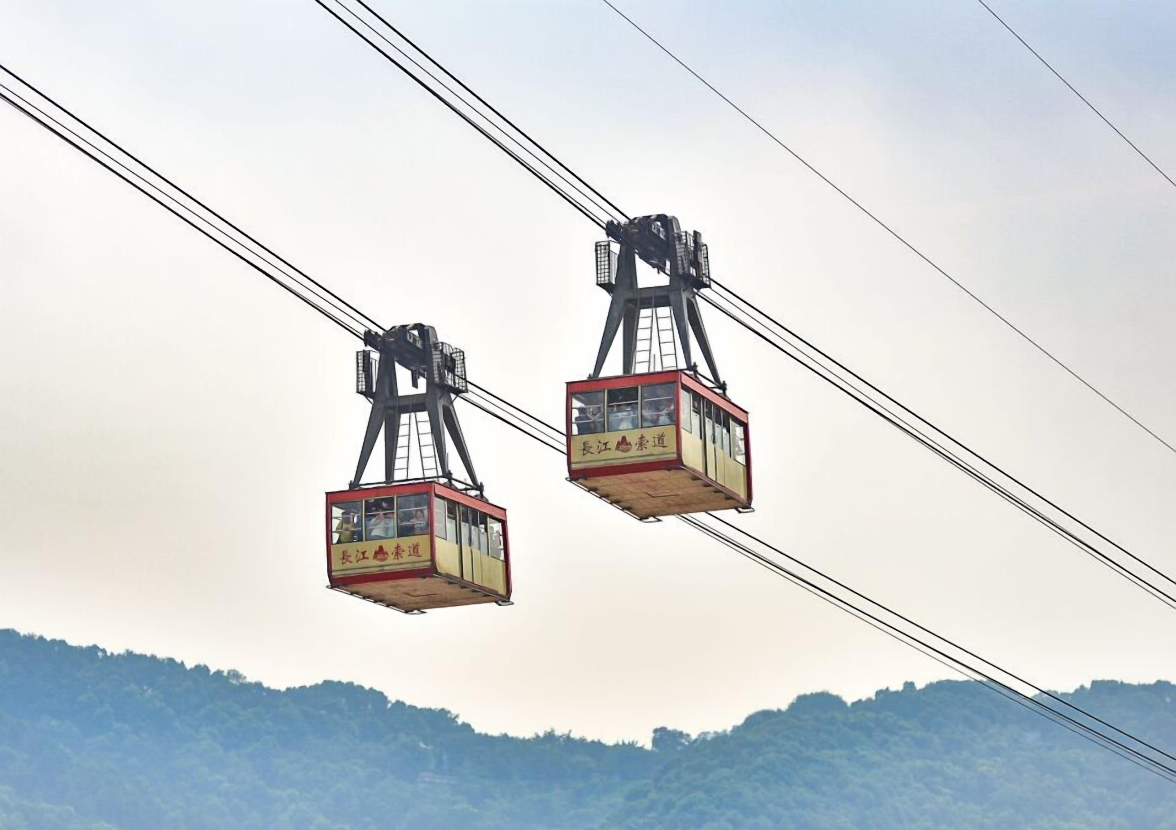Two cable cars suspended by cables against a backdrop of hills.