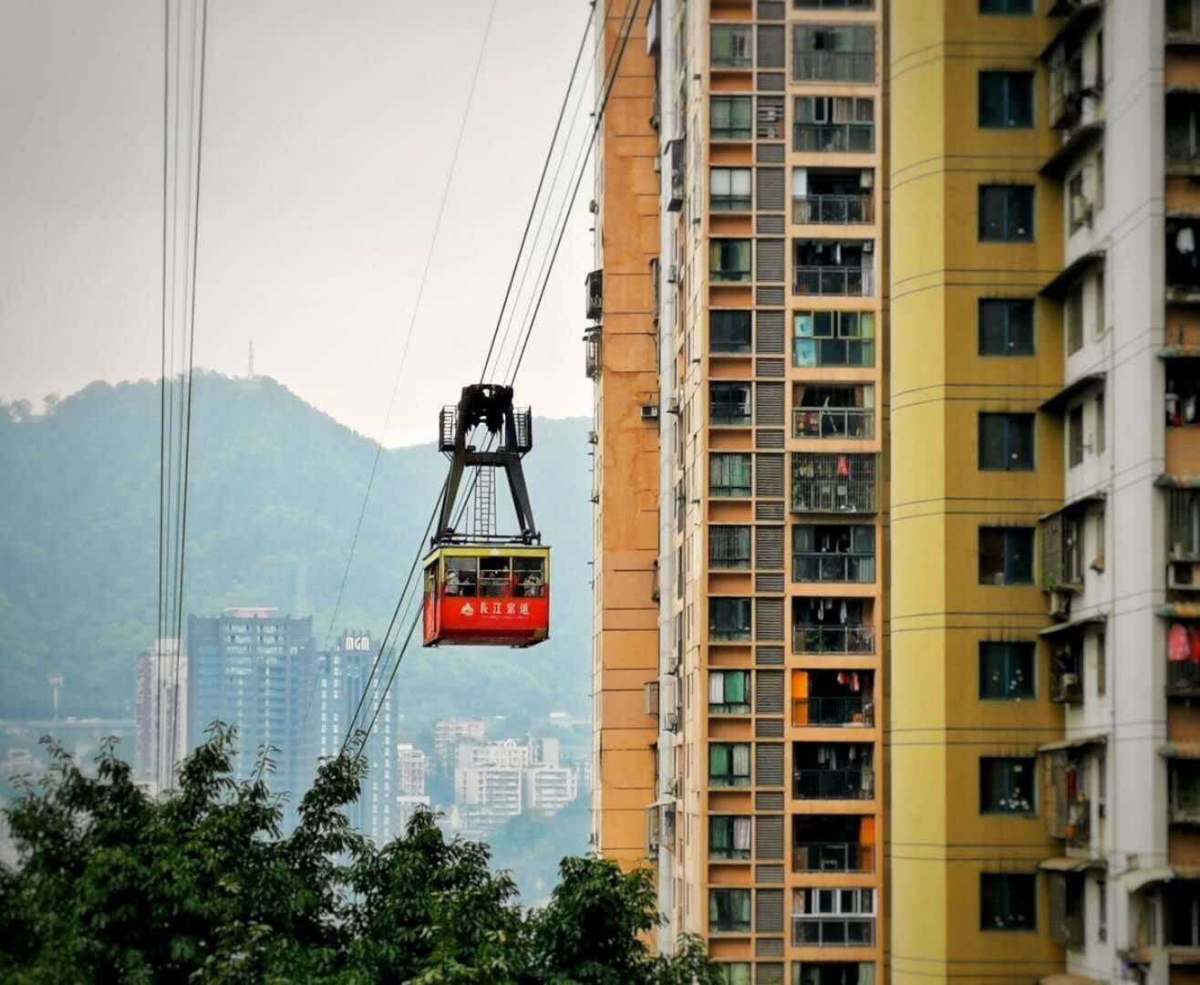 A cable car moving between high-rise buildings with a mountainous backdrop.