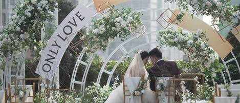 A wedding setup with a couple under an arch decorated with white flowers and geometric shapes.