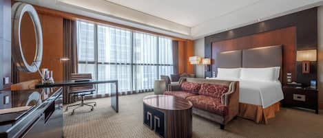 Habitación de hotel con una cama grande, un escritorio, una silla, una mesa redonda de centro y un ventanal con cortinas.