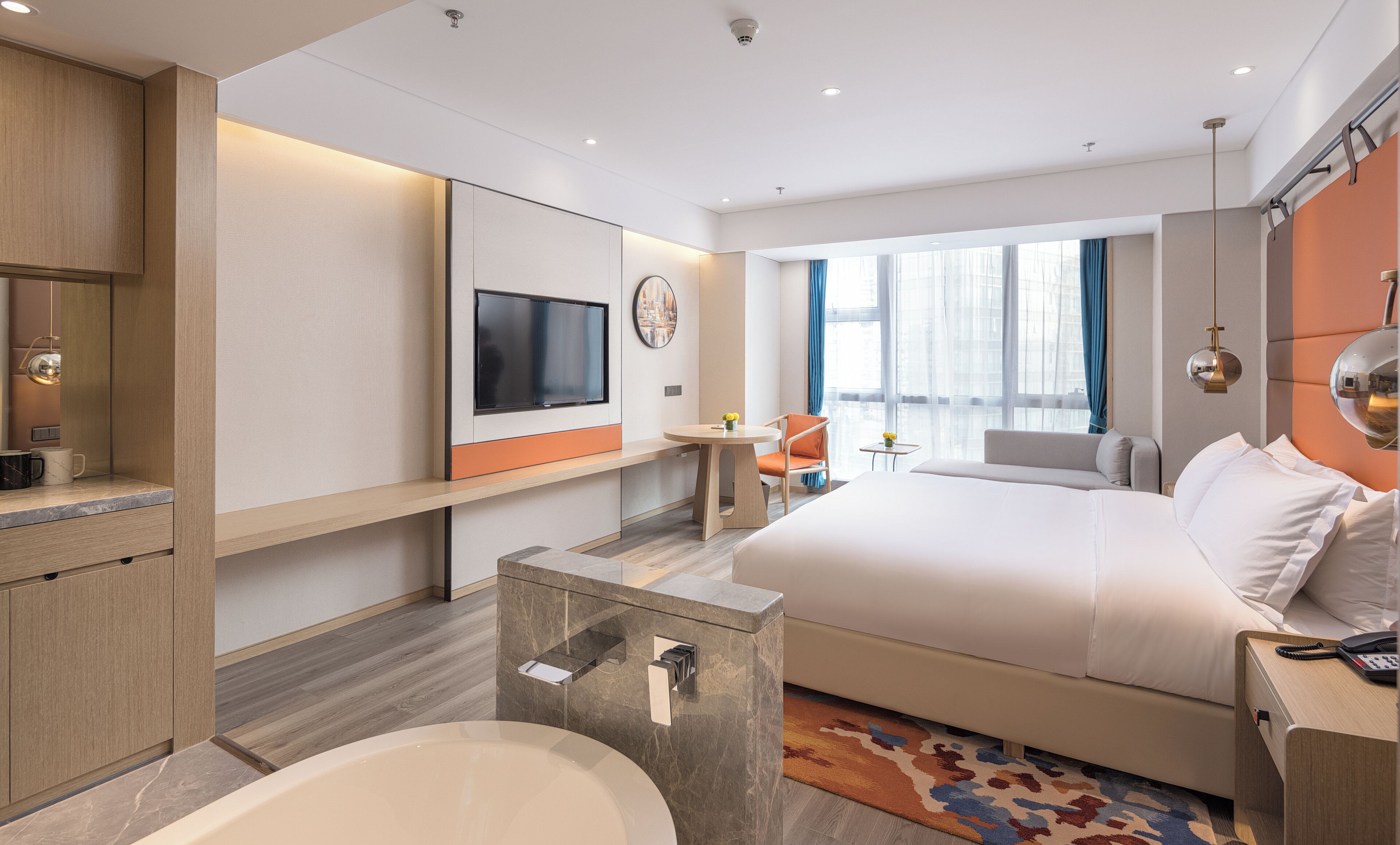 A modern hotel room with a large bed, a TV, a desk, and a bathroom with a bathtub.