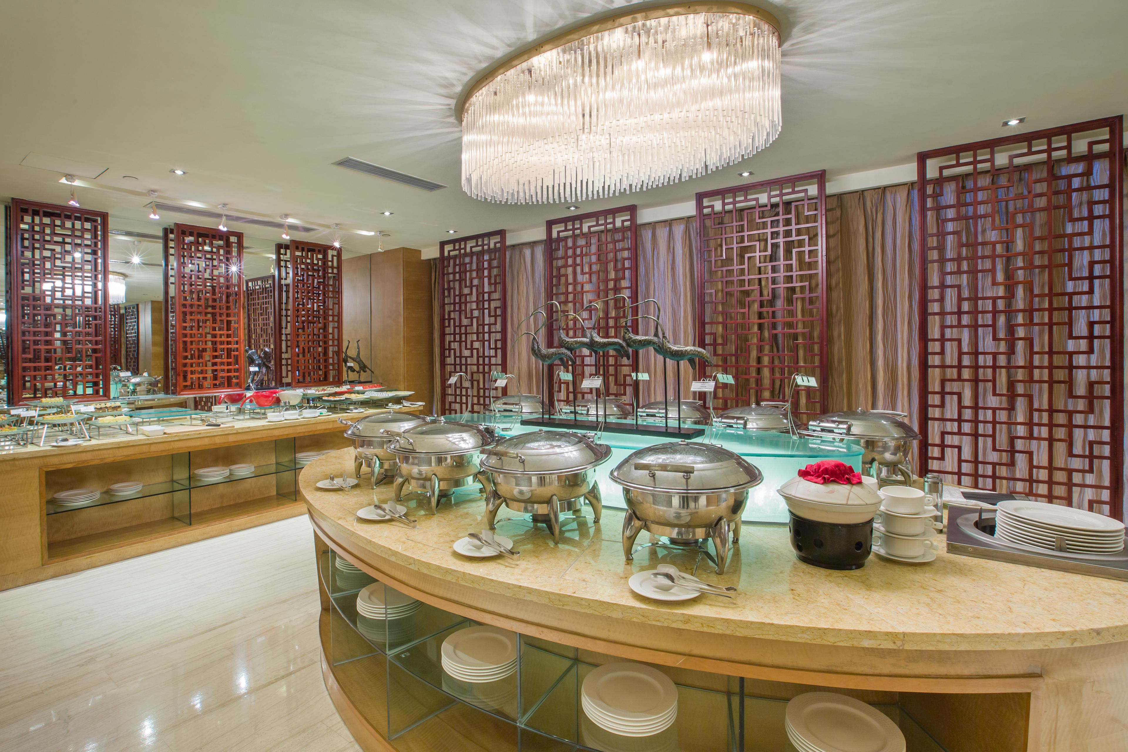 A buffet setup with multiple serving stations, glassware, and a decorative ceiling light.
