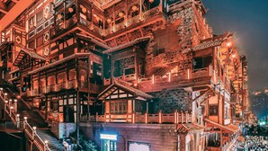 A traditional multi-story building with intricate wooden balconies and railings, a signboard, and a staircase leading to the entrance.