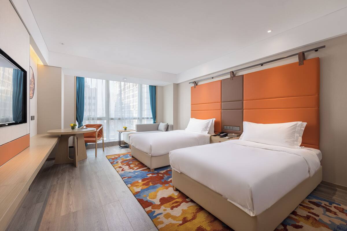 A hotel room with two beds, a desk, and a chair.