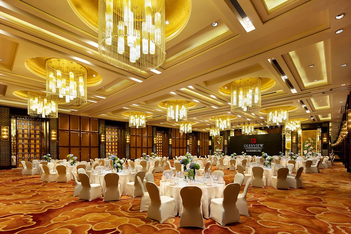Un salón de banquetes con mesas redondas dispuestas para eventos, candelabros y un escenario con un banderín.