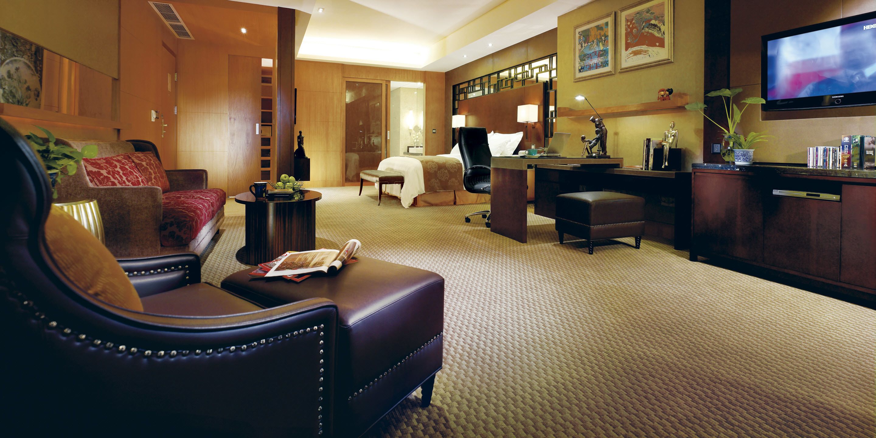 A hotel room with a leather armchair, a bed, a desk, and a television.