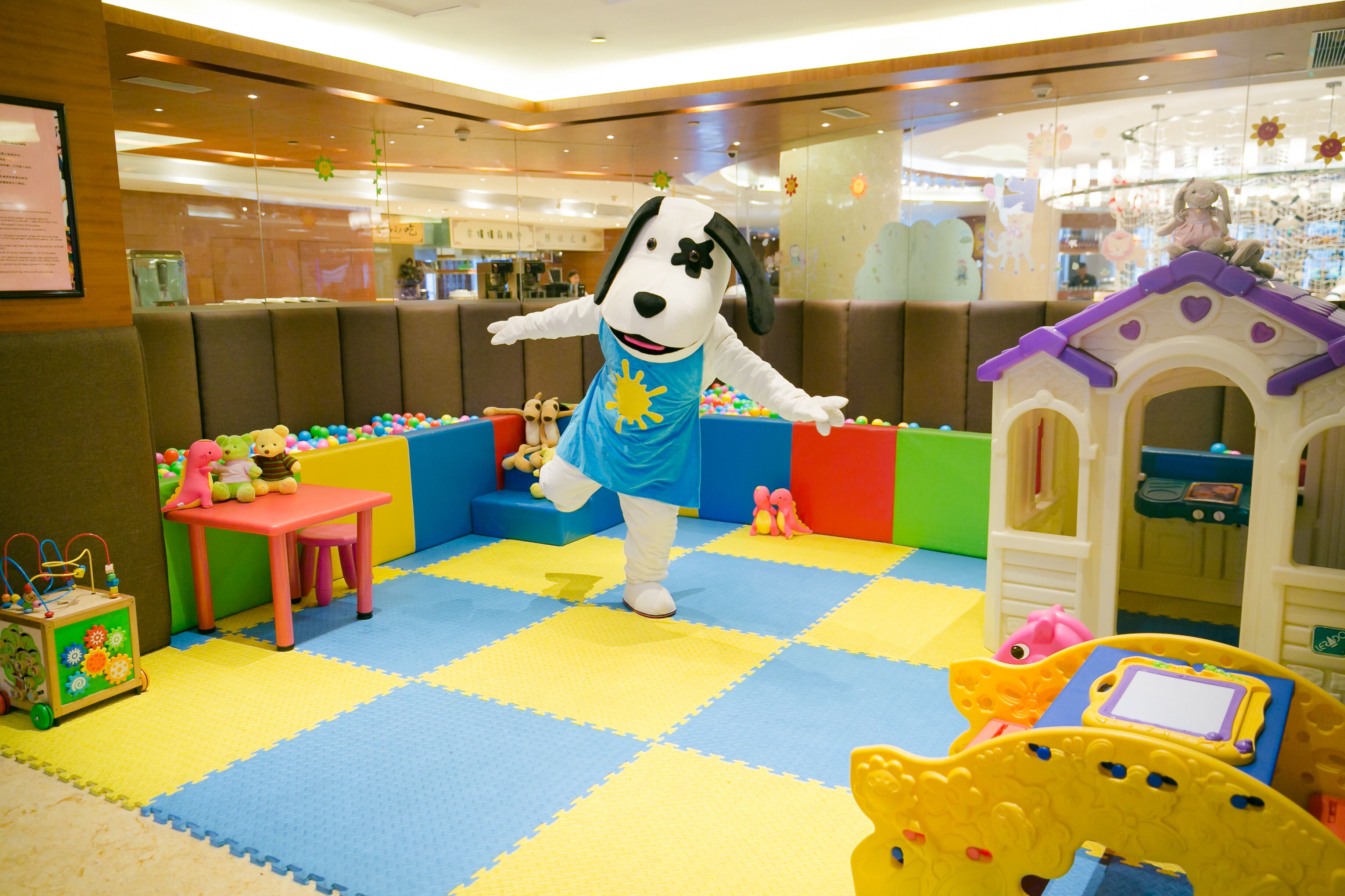 Un espace de jeux avec une grande mascotte canine, une maison de jeu et une piscine à balles.