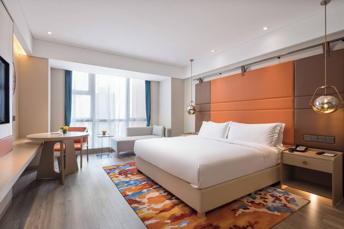 A modern hotel room with a large bed, a desk, a chair, and a small table with a vase of flowers.