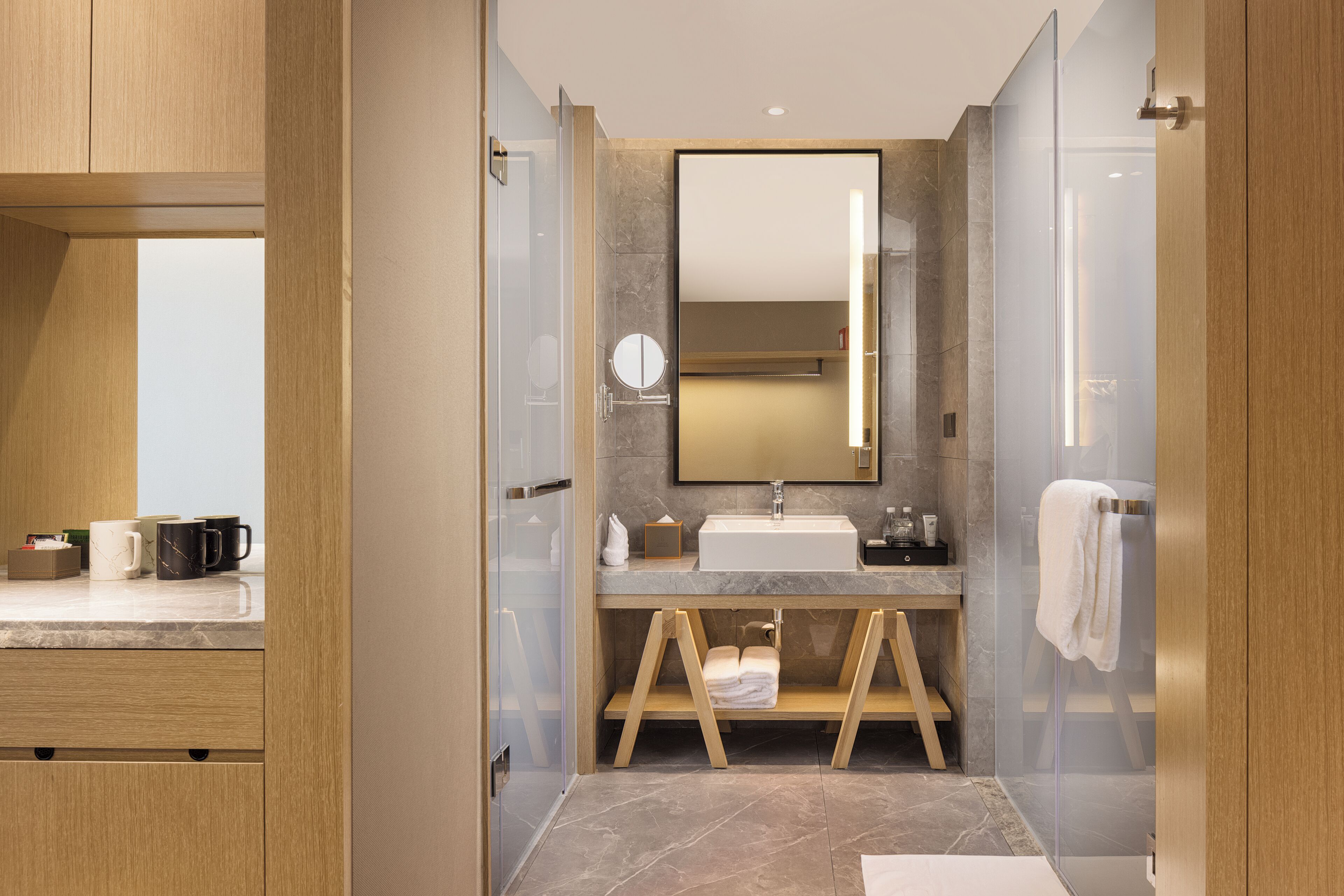 A modern bathroom with a glass shower enclosure, a wooden vanity, and a large mirror.