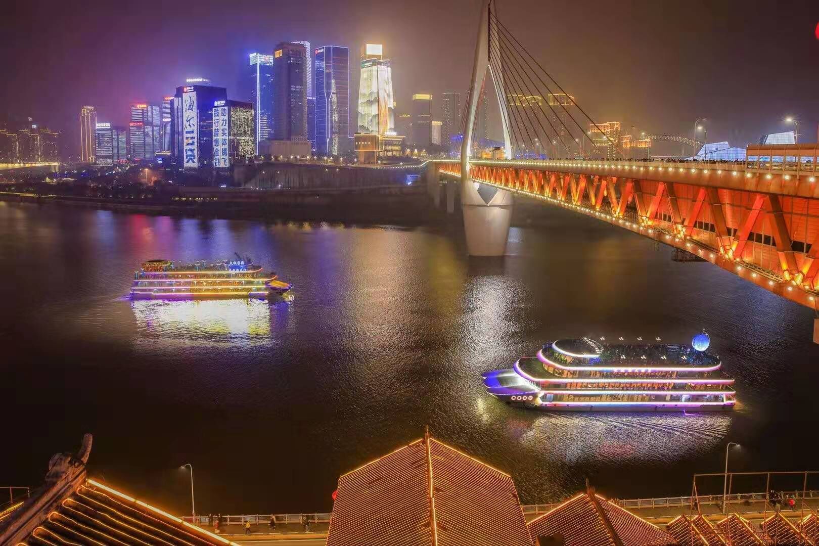 A nighttime cityscape with illuminated buildings and a bridge over a river.
