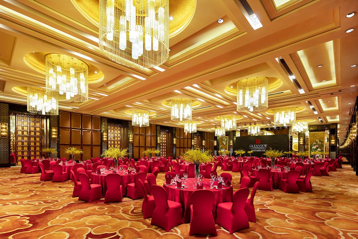 A banquet hall with round tables, red chairs, and chandeliers.