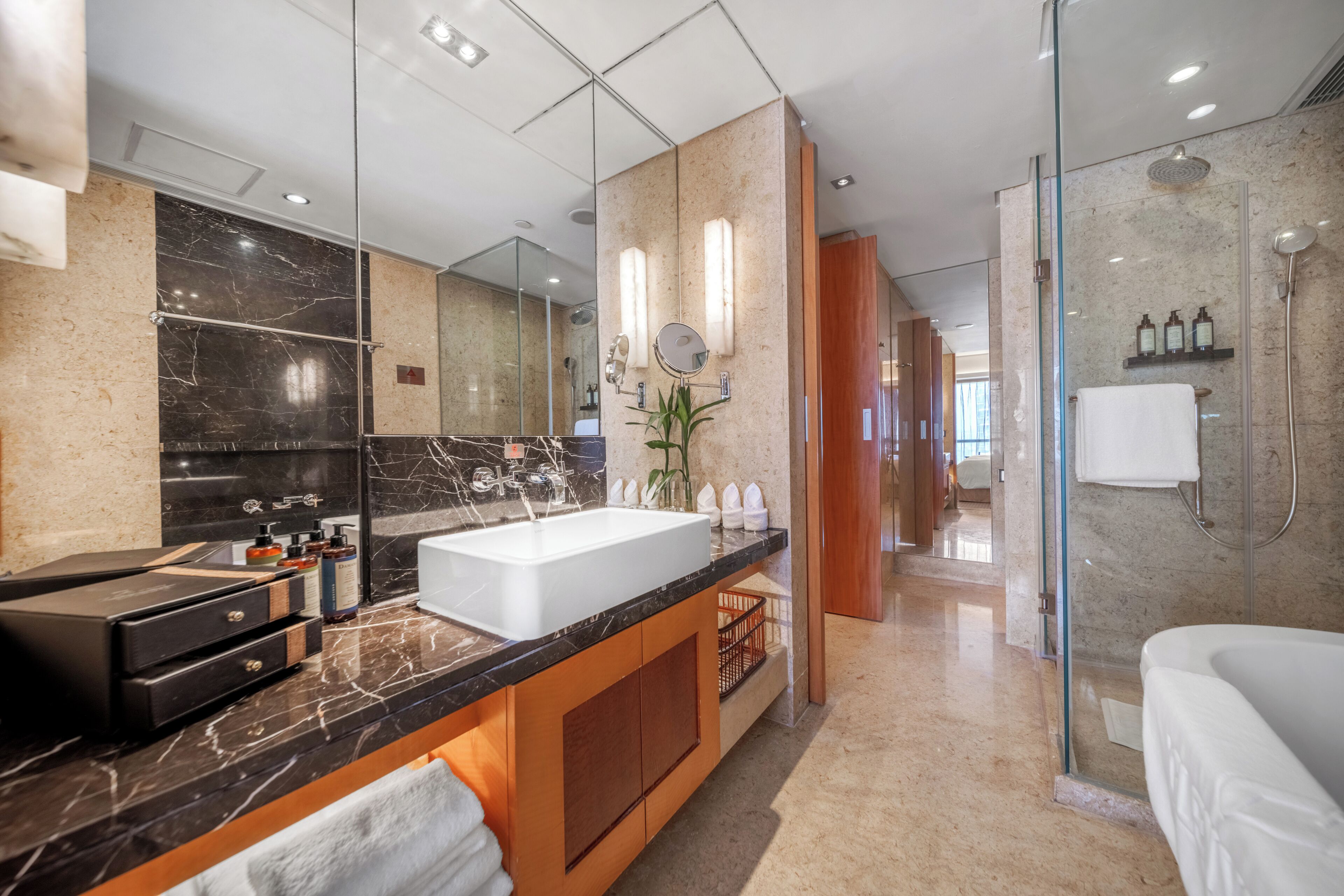 Un baño moderno con un espejo grande, un lavamanos blanco y una zona de ducha con paredes de vidrio.