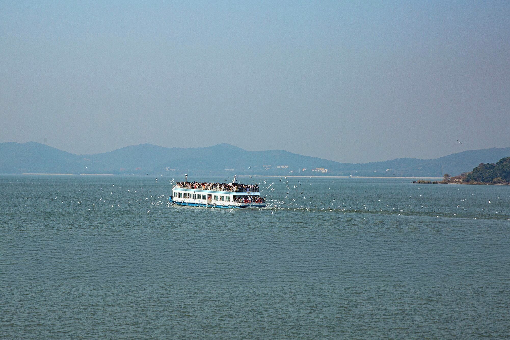 A boat with passengers on a calm body of water, surrounded by mountains and a clear sky.