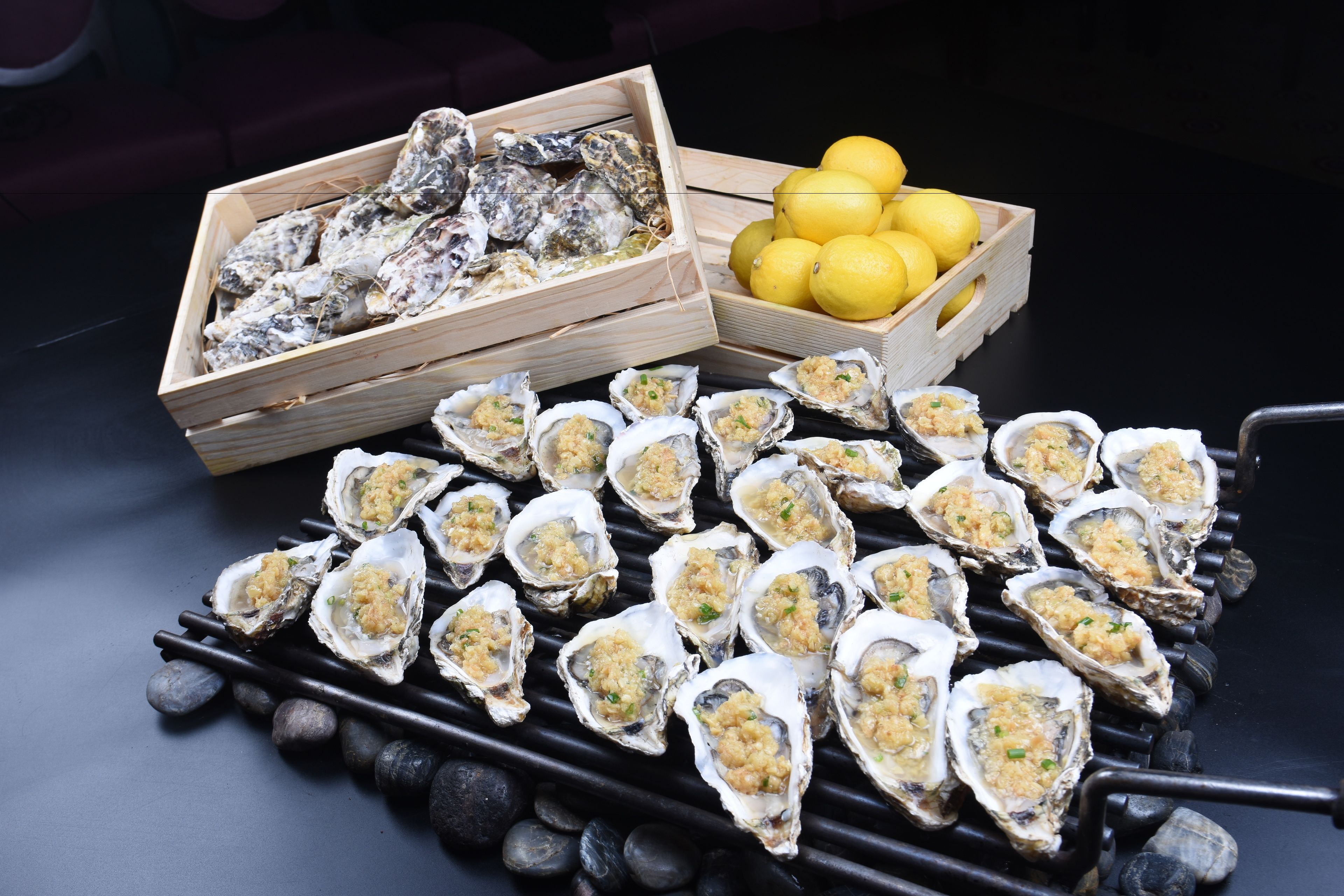 A variety of oysters on a tray, a wooden box with oysters, and a wooden crate with lemons.