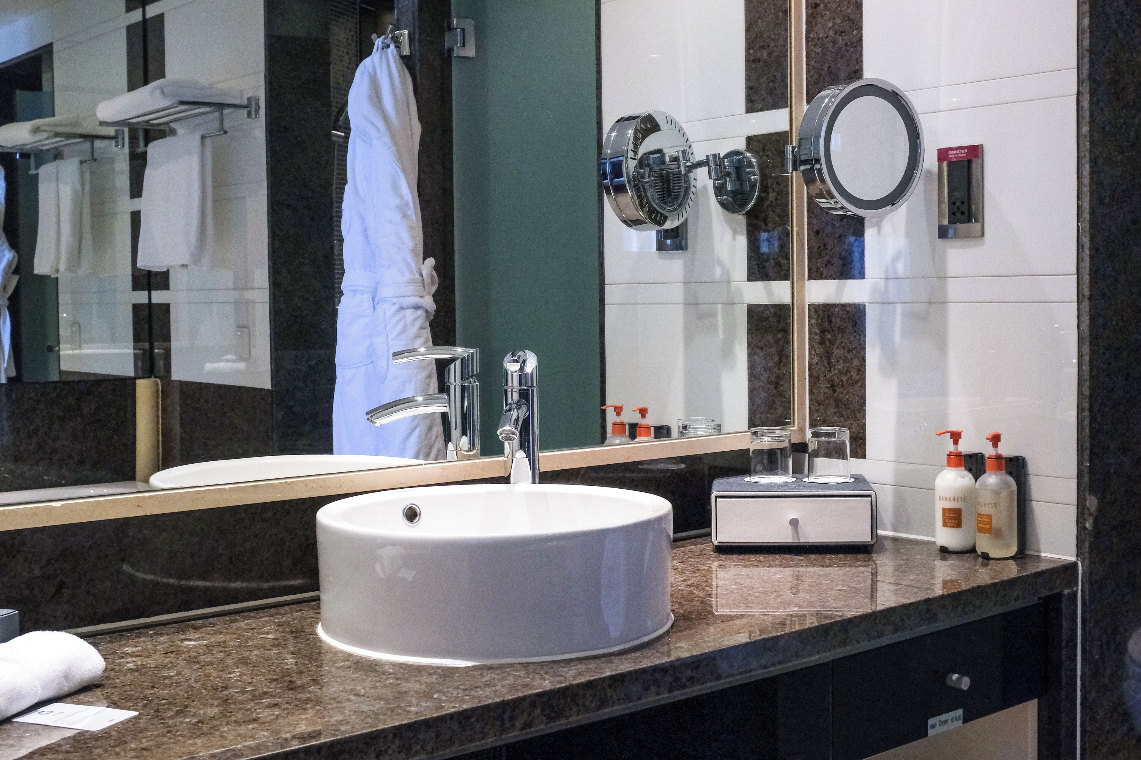 A modern bathroom with a large mirror, two sinks, a towel rack, and toiletries.