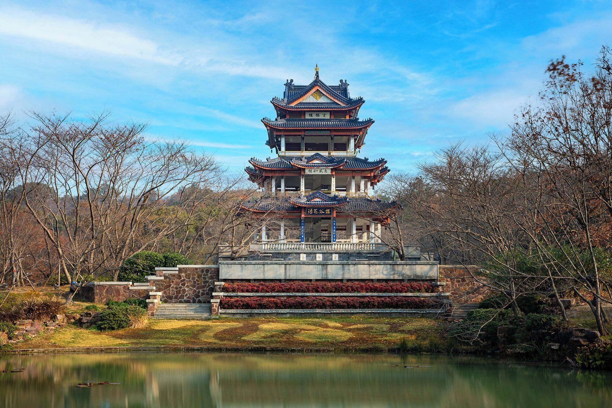 A traditional multi-tiered pagoda with a stone base and a pond in front.