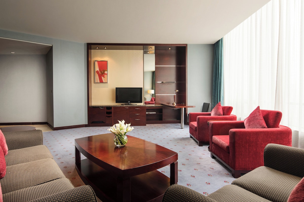 A hotel room with a seating area, a television, and a desk.