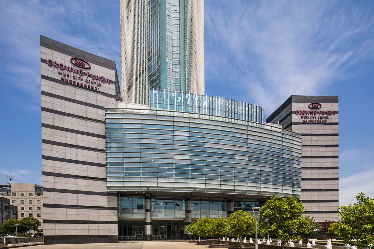 A modern building with a curved glass facade, labeled "Crowne Plaza Wuxi City Center."