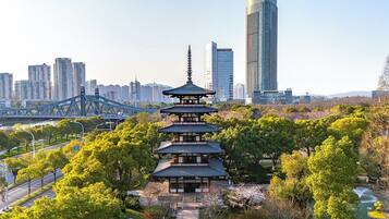 Una pagoda tradicional rodeada de exuberante vegetación, con un paisaje urbano moderno y un puente al fondo.