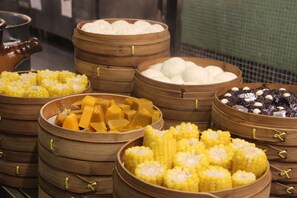 Diversos alimentos en vaporeras de bambú, como mazorcas de maíz, arroz blanco y otros platos.