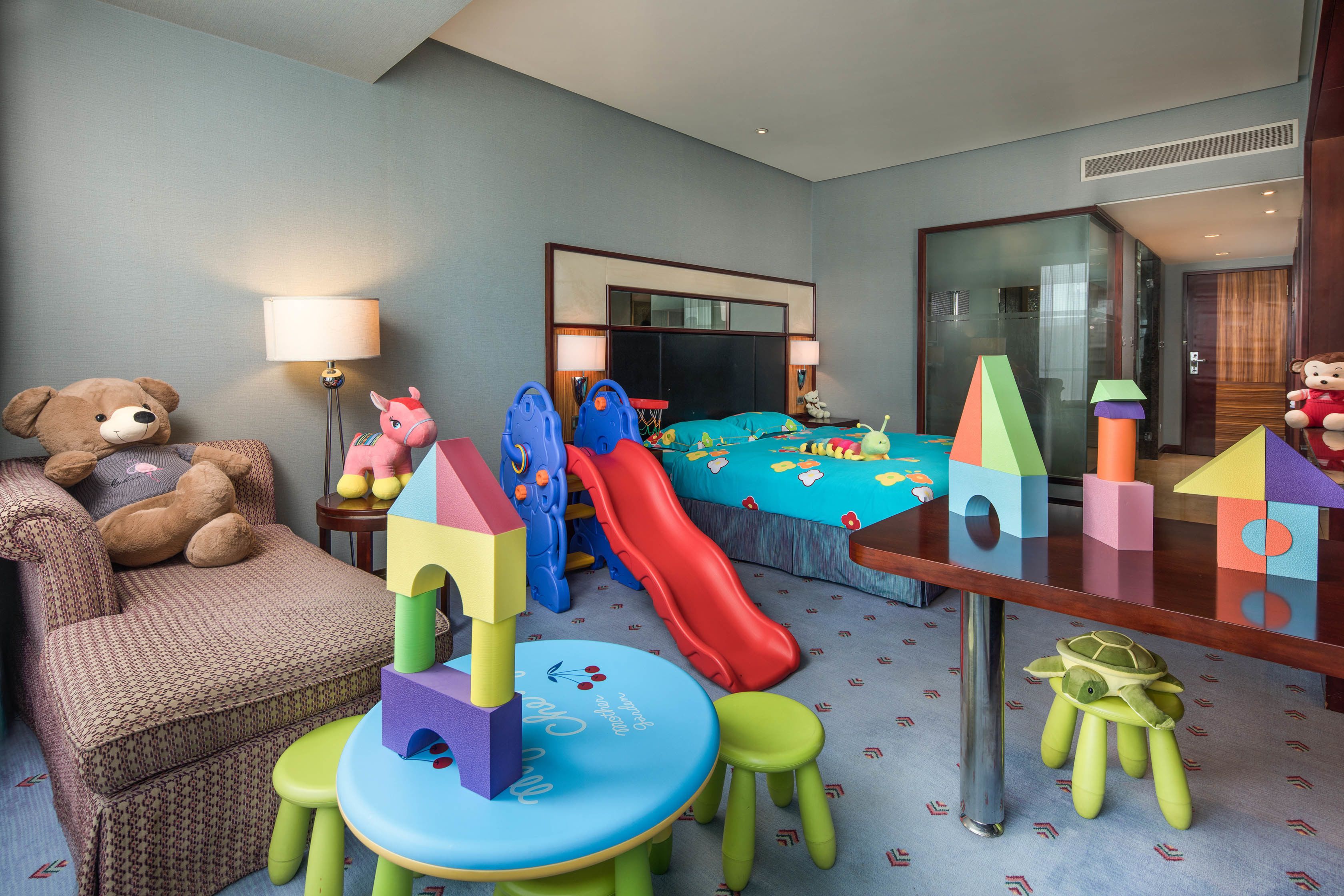 A children's playroom with a bed, a teddy bear, a slide, and various toys.
