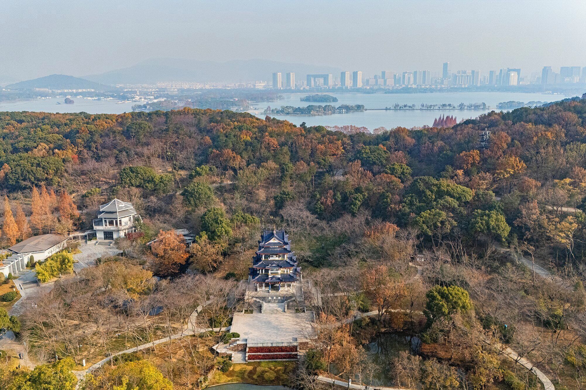 Ein traditioneller japanischer Tempelkomplex, umgeben von Herbstlaub, mit einer Stadtkulisse im Hintergrund.