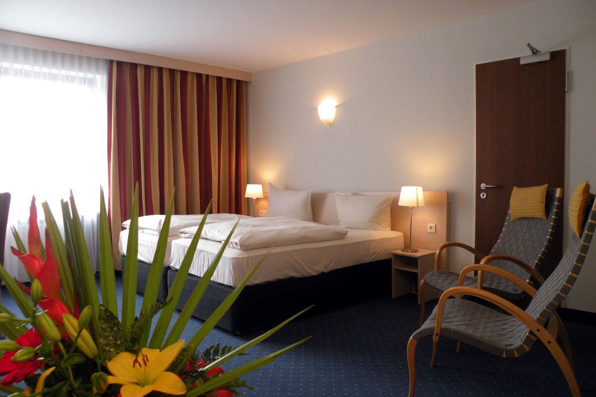 A hotel room with a bed, two bedside lamps, a wooden chair, and a door.