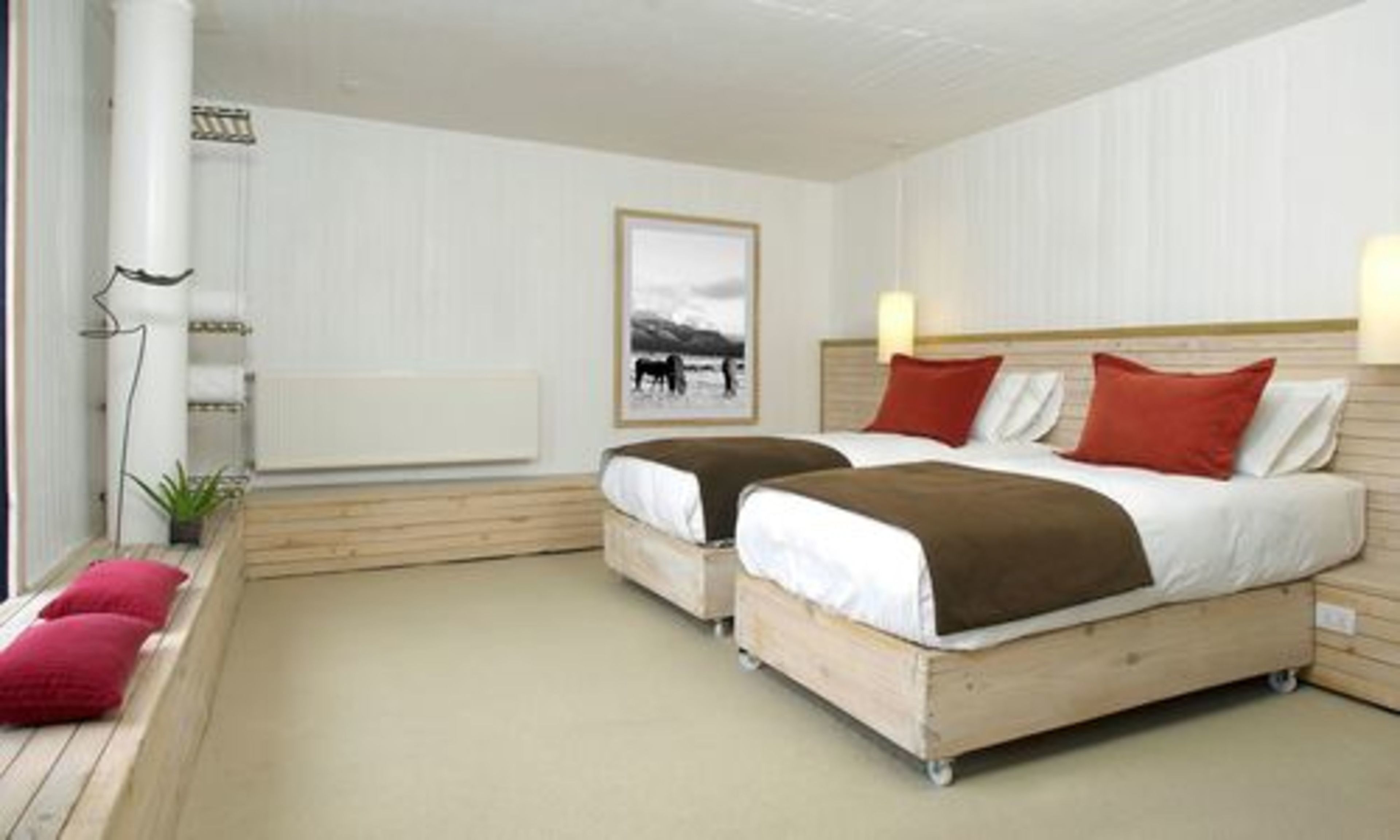 A bedroom with two beds, a radiator, a framed picture on the wall, and a potted plant.