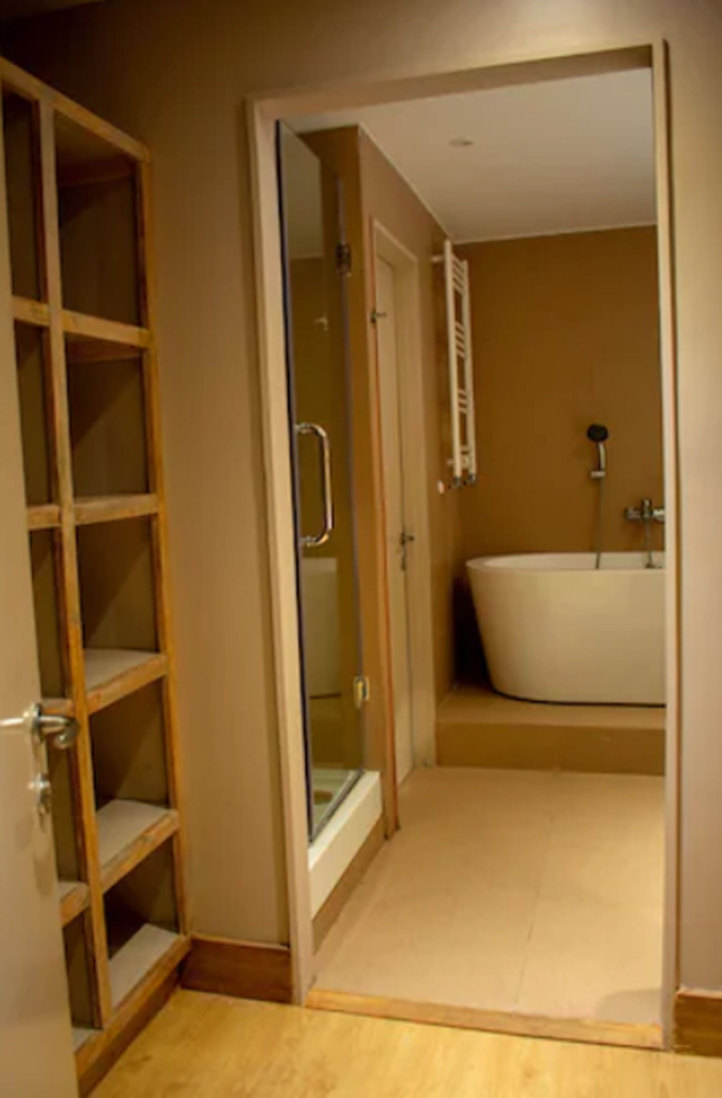 A bathroom with a bathtub, a shower, and a wooden shelving unit.