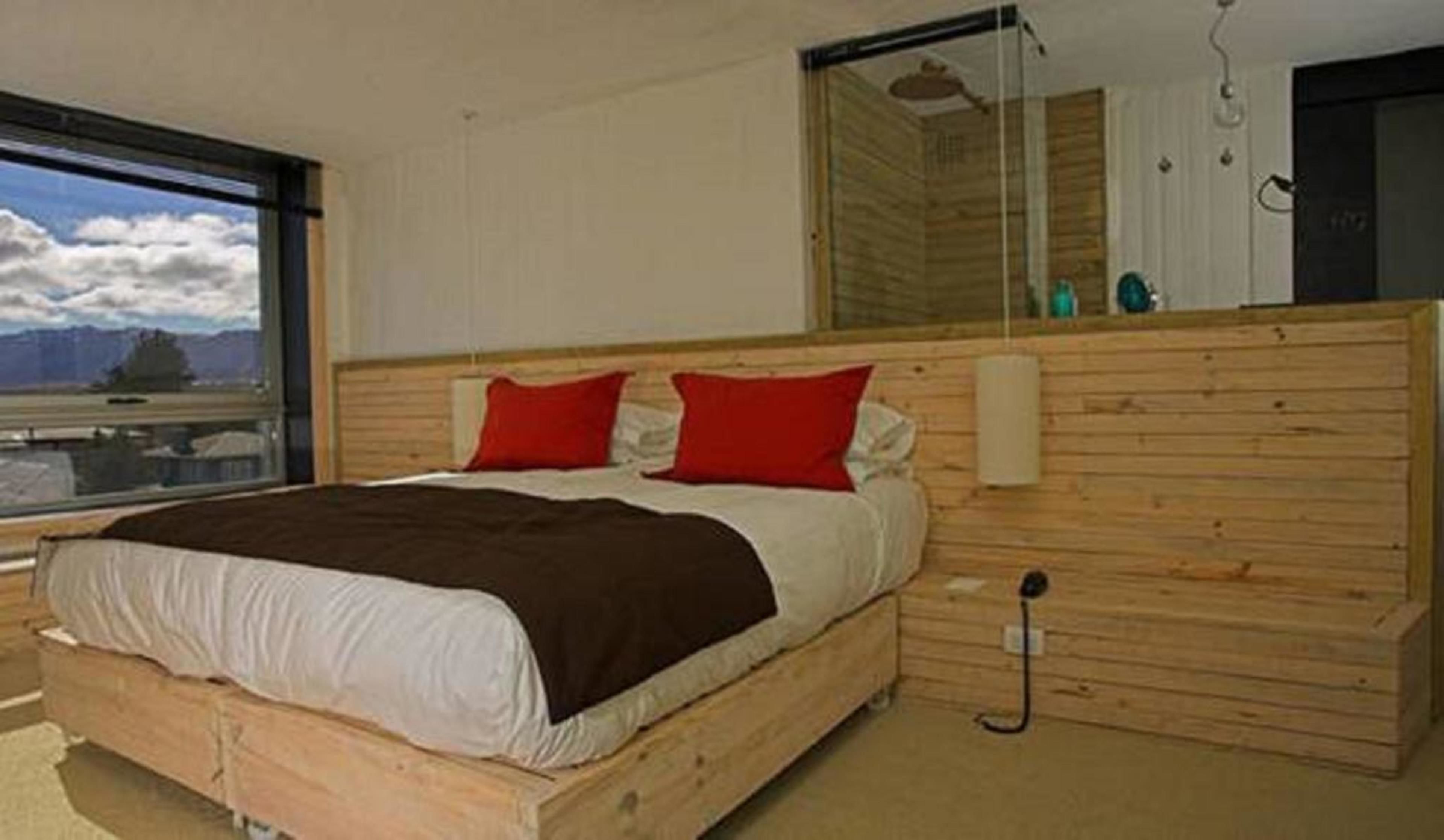 A bedroom with a wooden headboard, a large window, and a view of the sky.