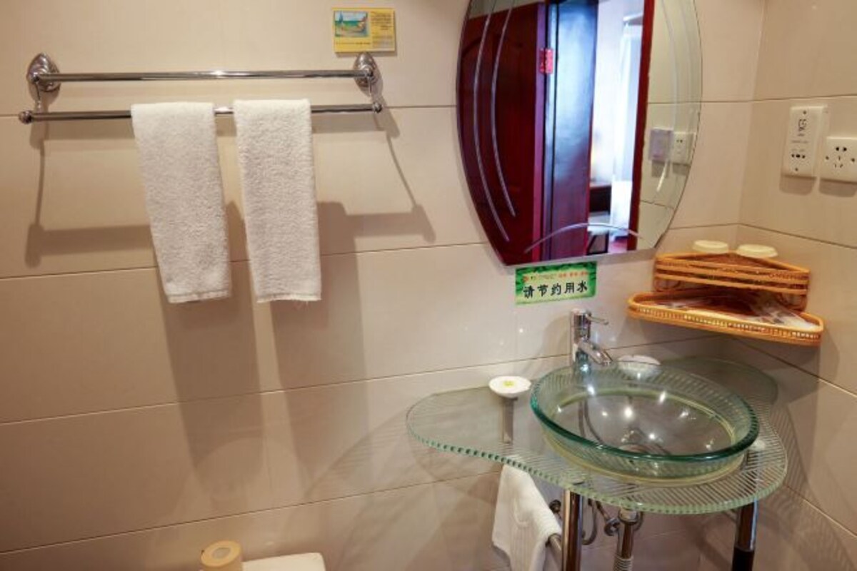 Une salle de bain avec un lavabo en verre, un porte-serviettes avec deux serviettes, un miroir et une petite étagère contenant des articles de toilette.