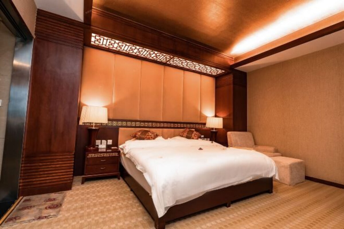 Une chambre d’hôtel avec un grand lit, deux tables de chevet, une chaise et un panneau décoratif au plafond.