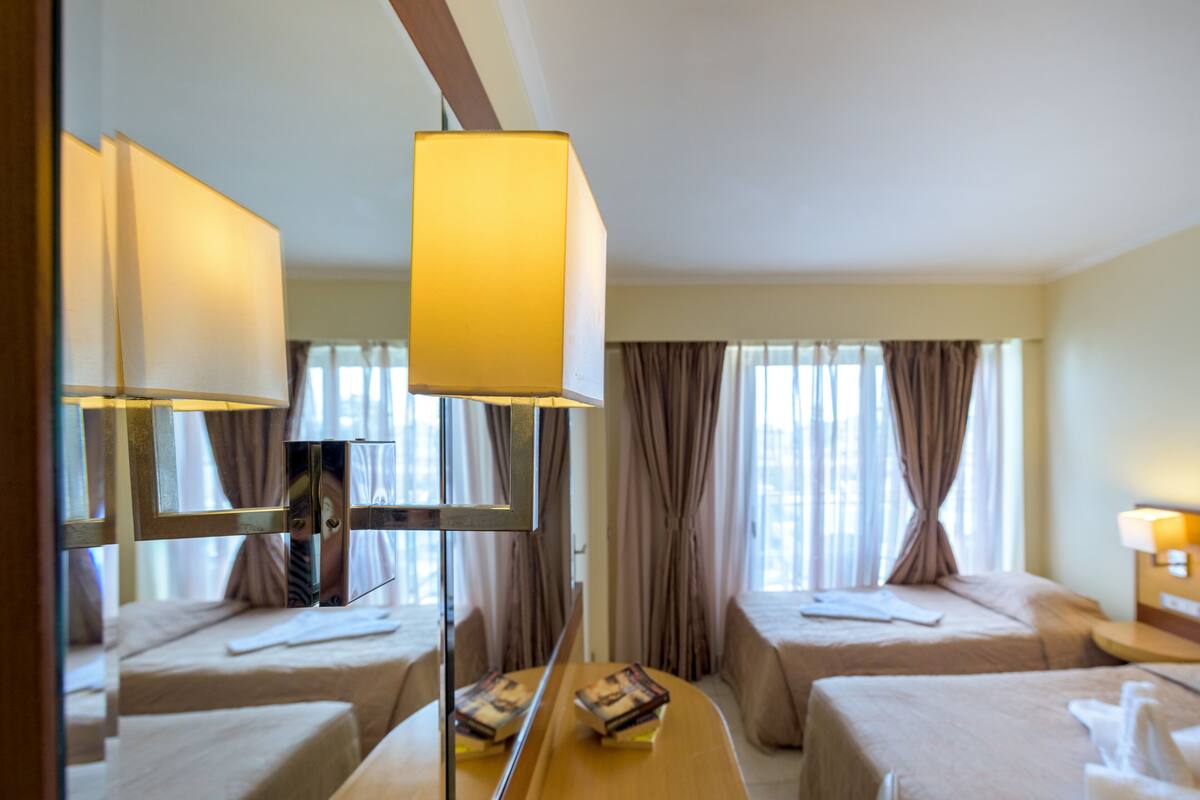 A hotel room with two beds, a mirror, and a bedside table with a lamp.