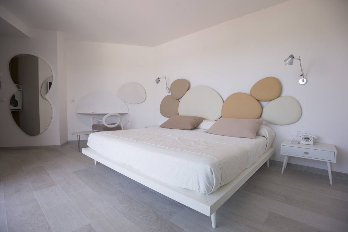 A modern bedroom with a bed, bedside tables, a mirror, and wall-mounted lighting.